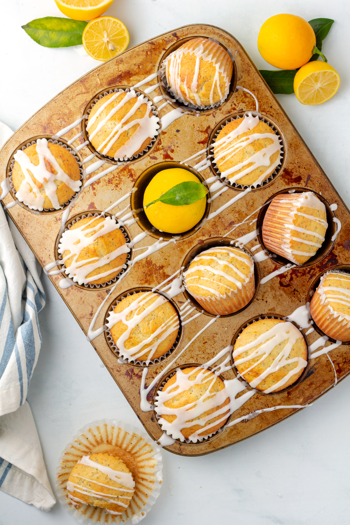 baked lemon poppy seed muffins In a muffin tin, with icing drizzled all across the muffins and tin