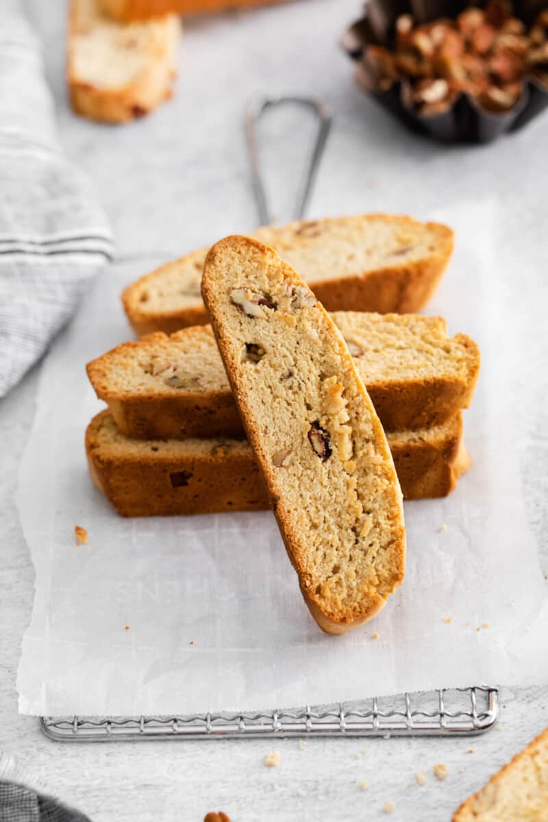 a single maple pecan biscotti leaning against a stack of biscotti on a parchment lined wire rack.