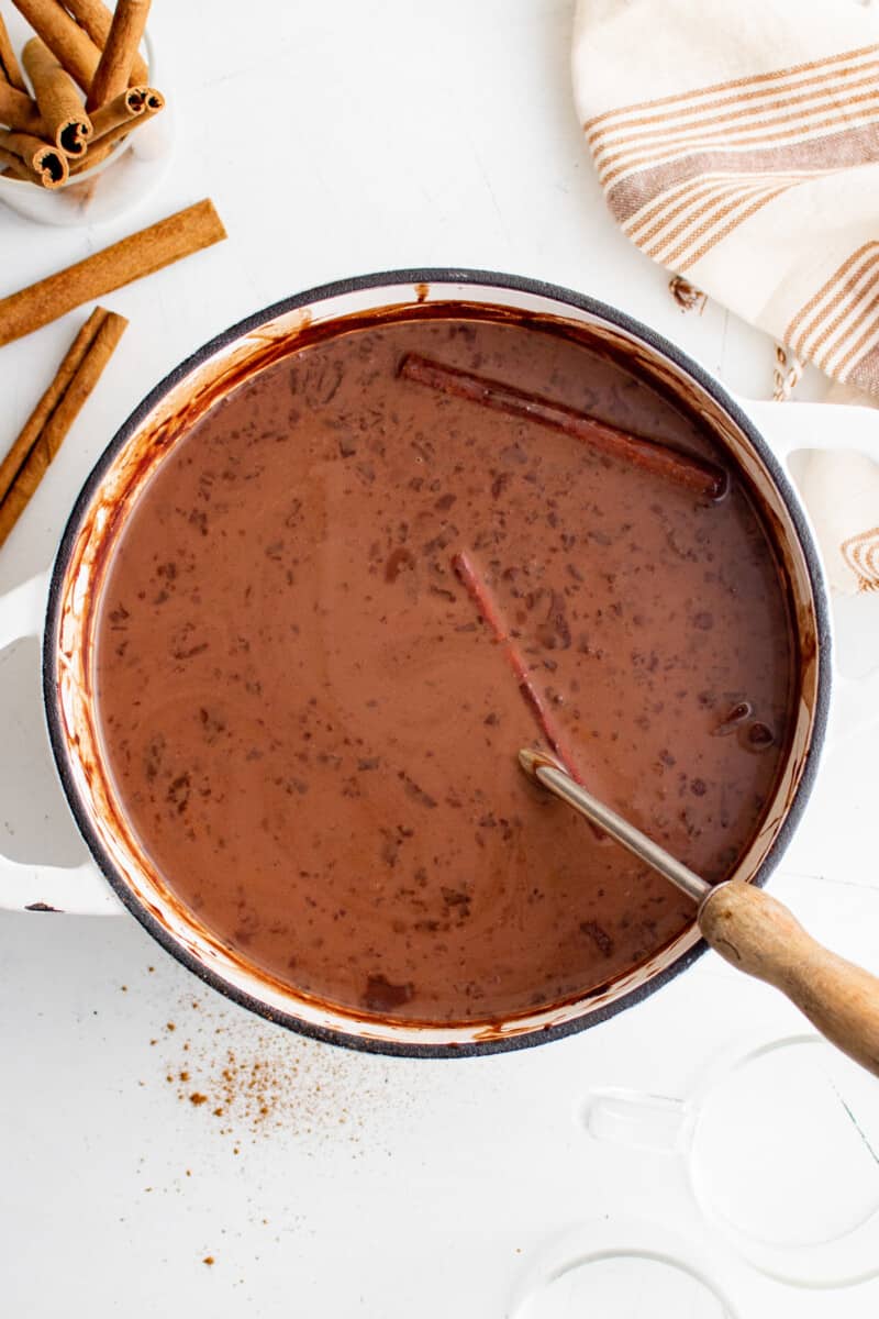 overhead view of mexican hot chocolate in a white dutch oven with a spoon.