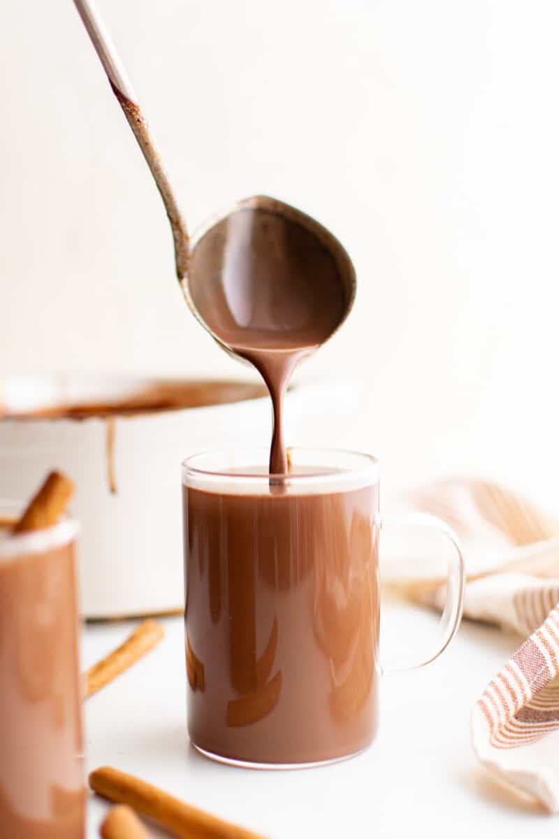 a ladle pouring mexican hot chocolate into a glass mug.