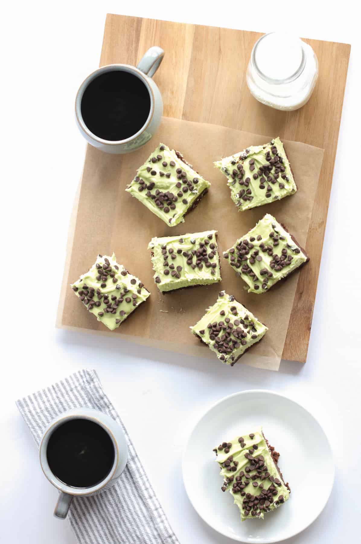 mint chocolate chip brownies on a cutting board and plate with cups of coffee