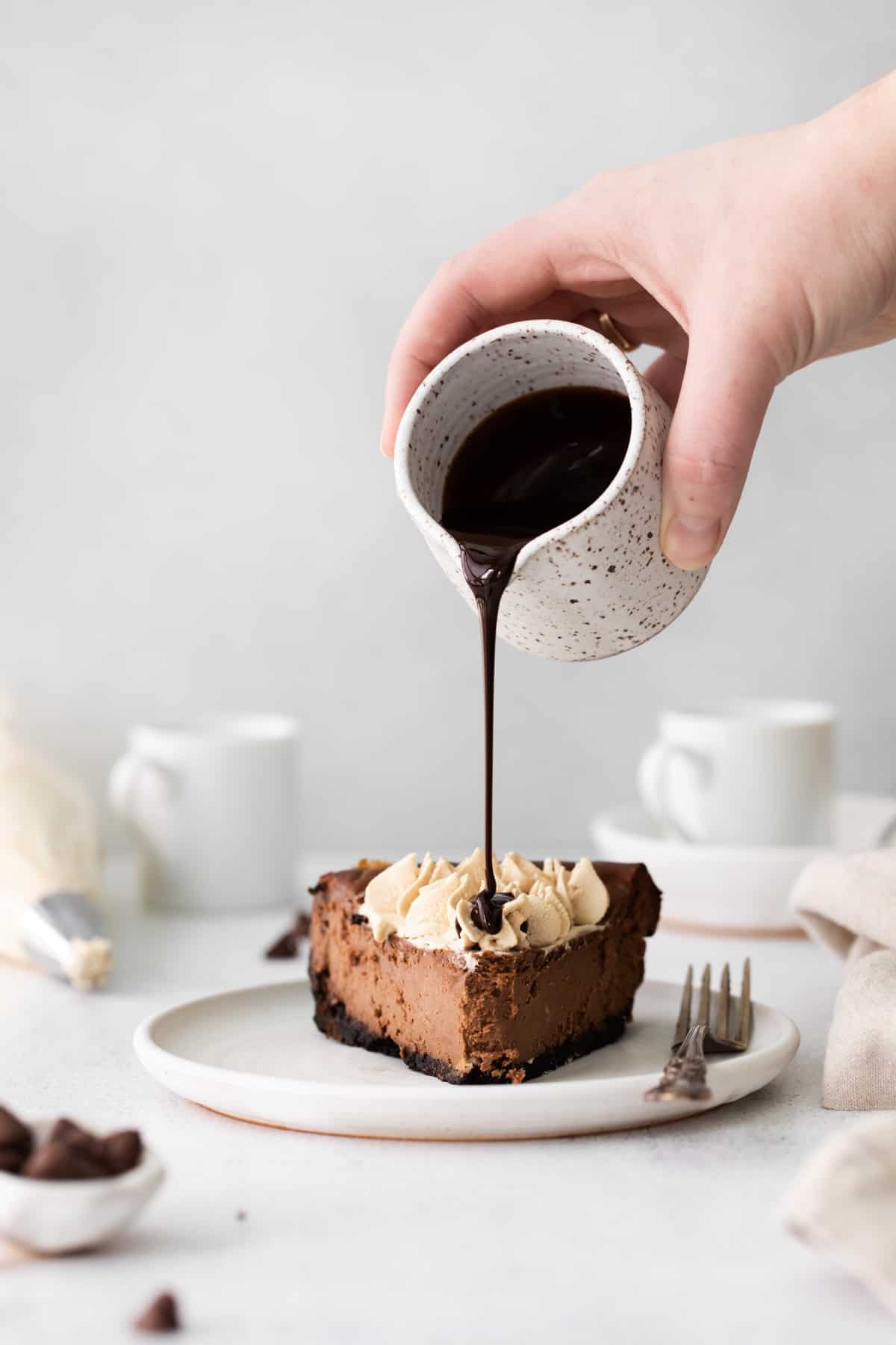 pouring chocolate over a slice of mocha cheesecake