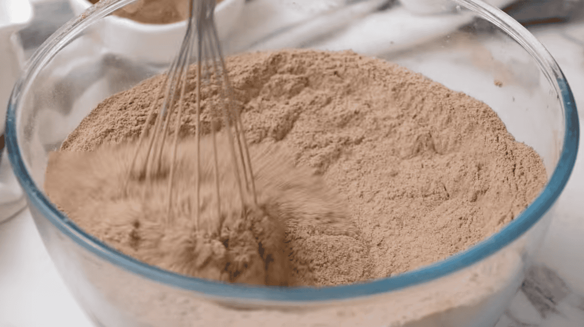 whisking dry ingredients for chocolate cake in a glass bowl.