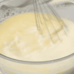 whisking creamy yellow liquid in a glass bowl.