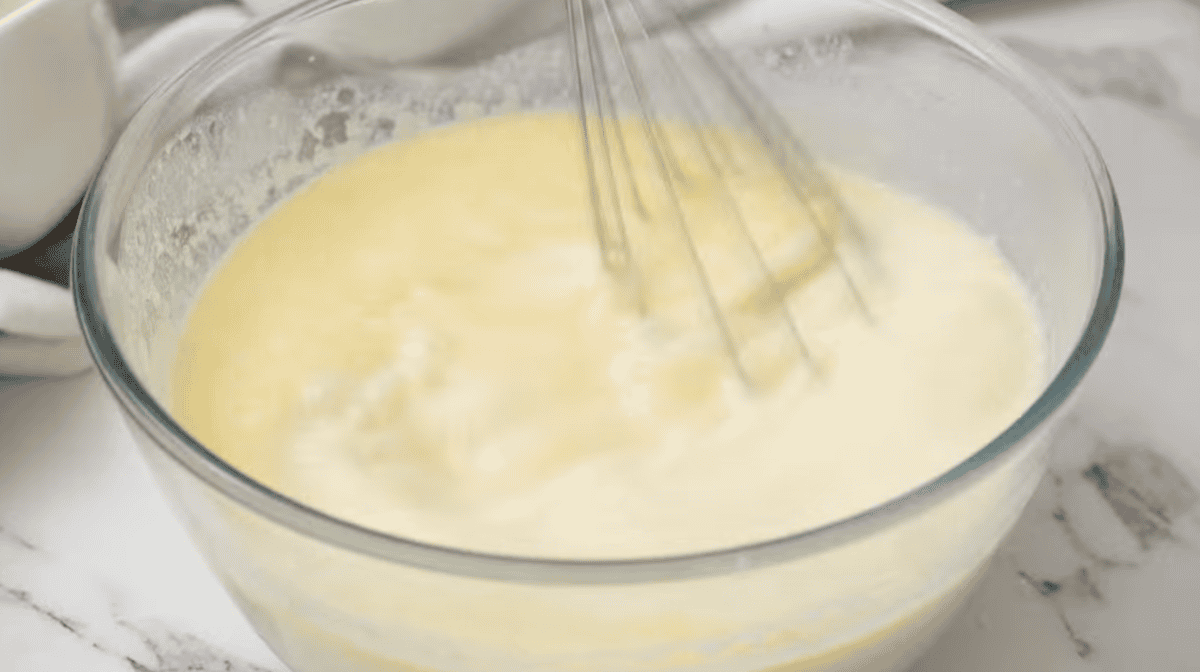 whisking creamy yellow liquid in a glass bowl.