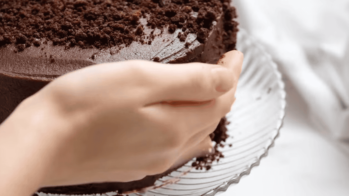 pressing chocolate cake crumbs onto a frosted cake.