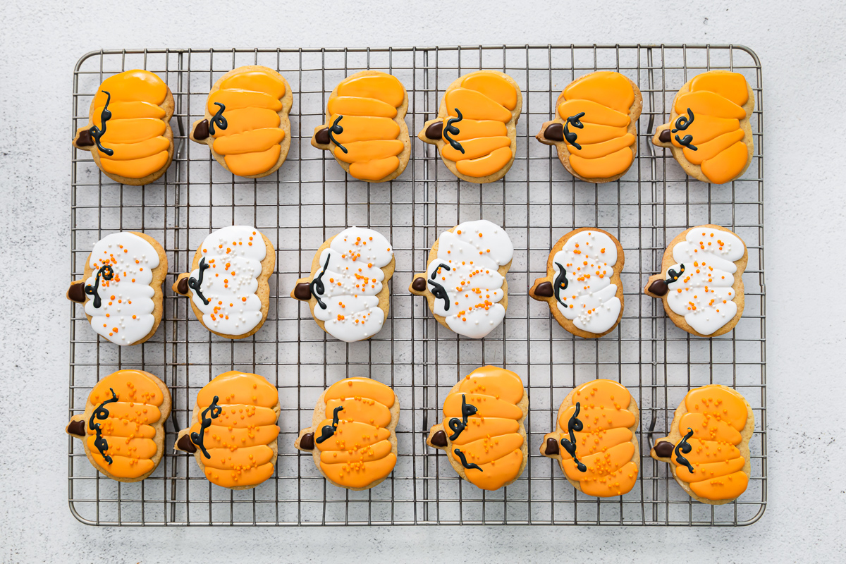frosted pumpkin sugar cookies lined up on a cooling rack