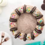 a frosted layered chocolate oreo cake topped with oreo cookies and rainbow sprinkles.