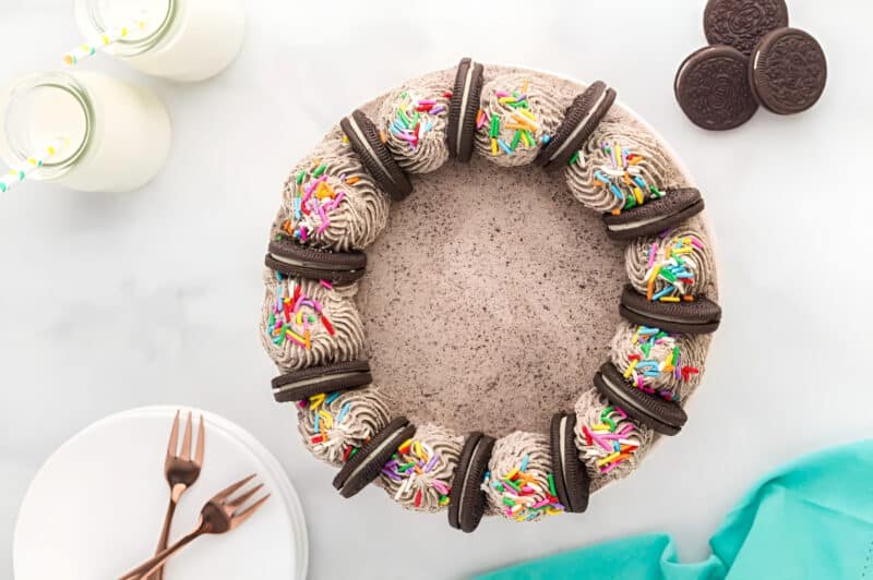 a frosted layered chocolate oreo cake topped with oreo cookies and rainbow sprinkles.