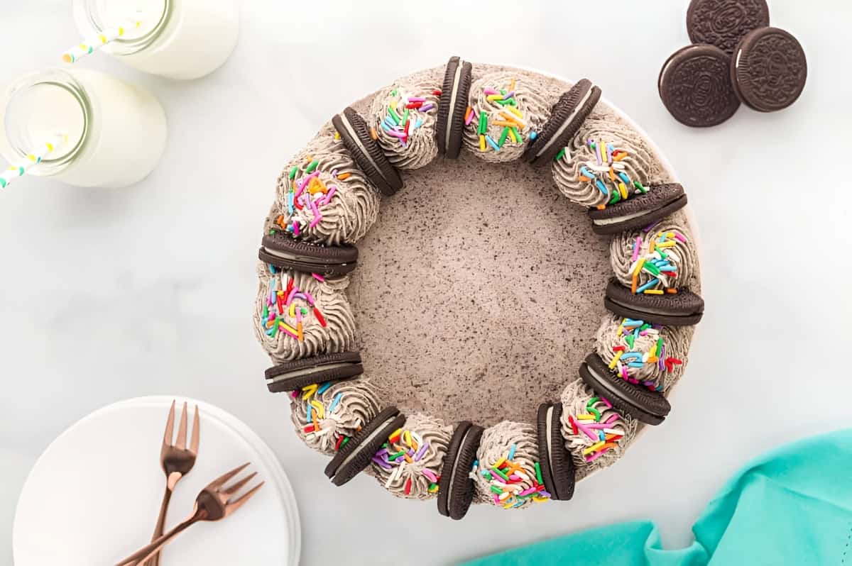 a frosted layered chocolate oreo cake topped with oreo cookies and rainbow sprinkles.