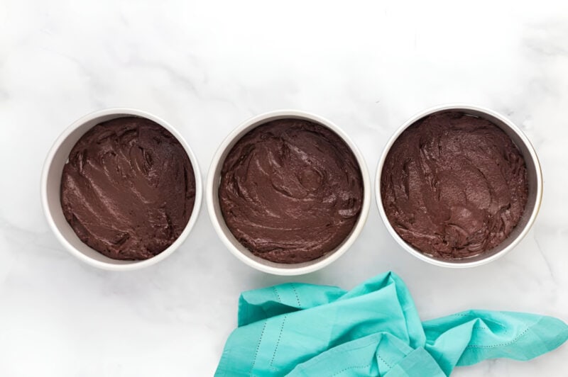 chocolate cake batter divided between three round cake pans.