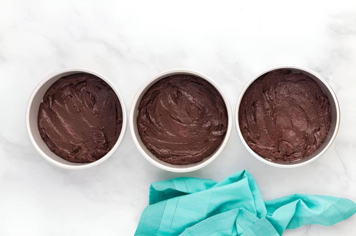 chocolate cake batter divided between three round cake pans.