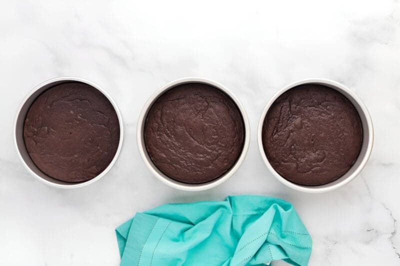 three baked chocolate cake layers in round cake pans.
