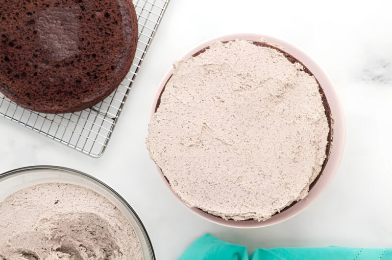 a layer of chocolate oreo cake topped with oreo buttercream on a cake stand.