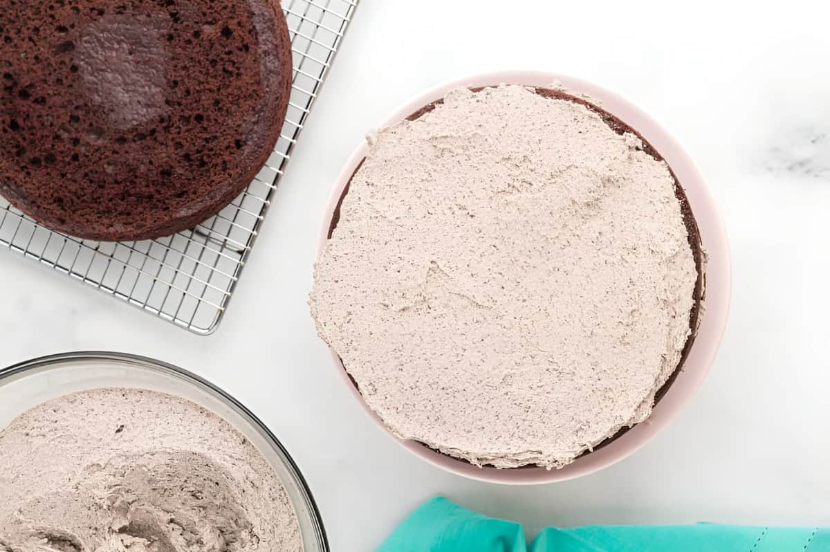 a layer of chocolate oreo cake topped with oreo buttercream on a cake stand.