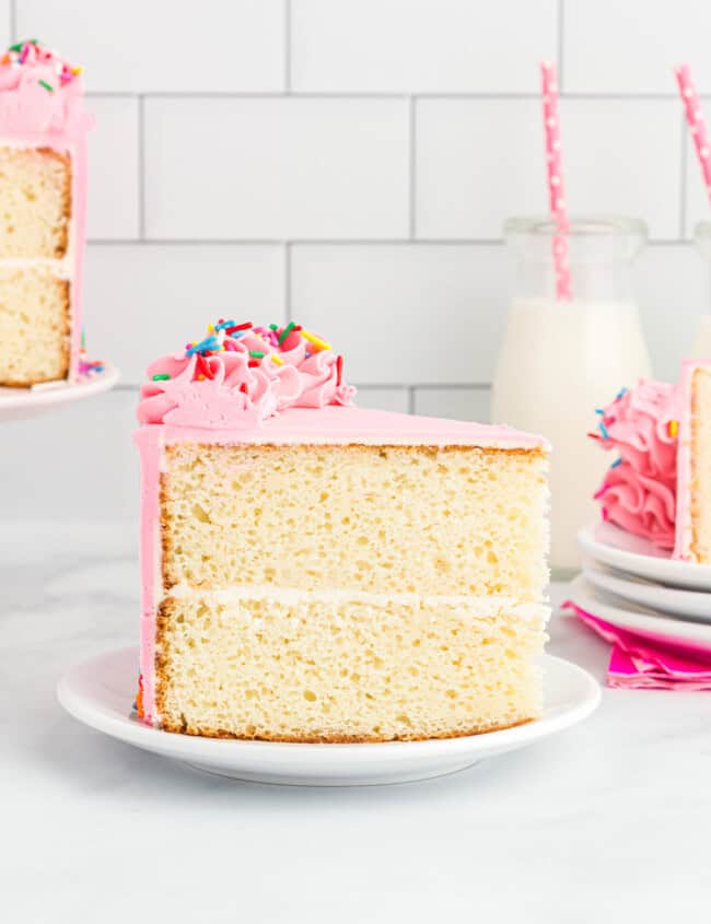 side view of a slice of doctored white cake mix cake on a white plate.