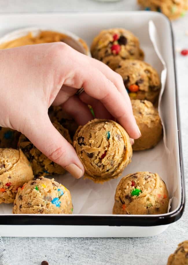 A hand grabbing a cookie from a baking sheet.