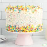 a rainbow sprinkle cake on a pink cake stand.