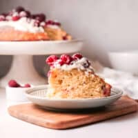 a slice of raspberry olive oil cake topped with whipped cream and fresh raspberries on a plate.