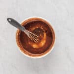 a whisk in a bowl of brown liquid.