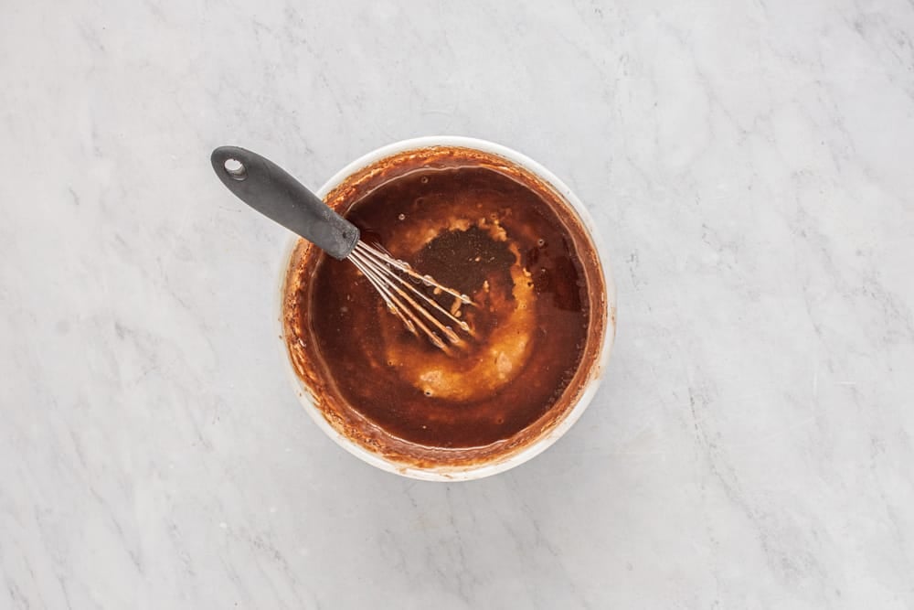 a whisk in a bowl of brown liquid.