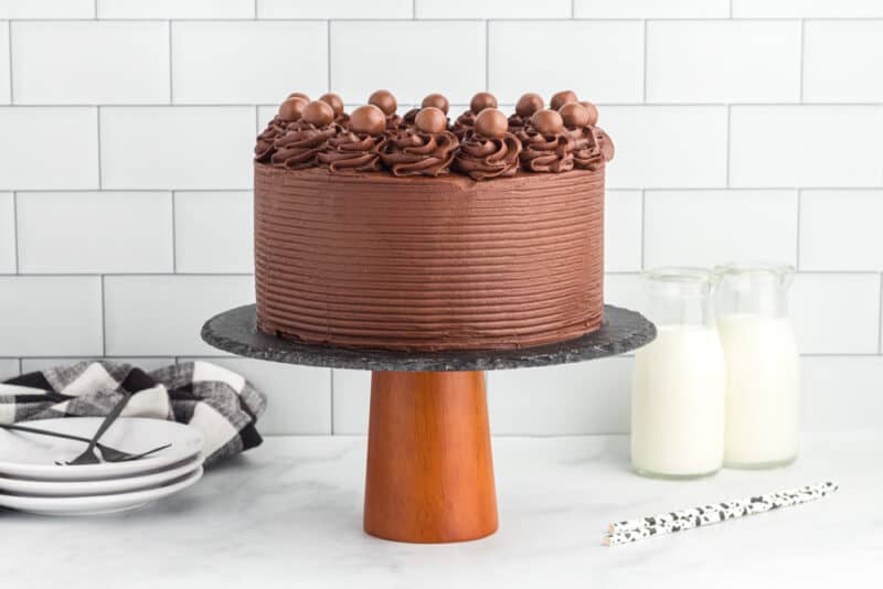 side view of frosted chocolate fudge cake on a cake stand.