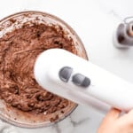 chocolate buttercream in a glass bowl with a hand mixer.