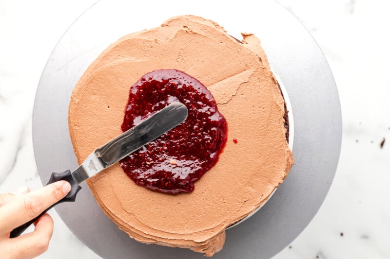 raspberry preserves spread over chocolate frosting and chocolate cake on a gray cake board.