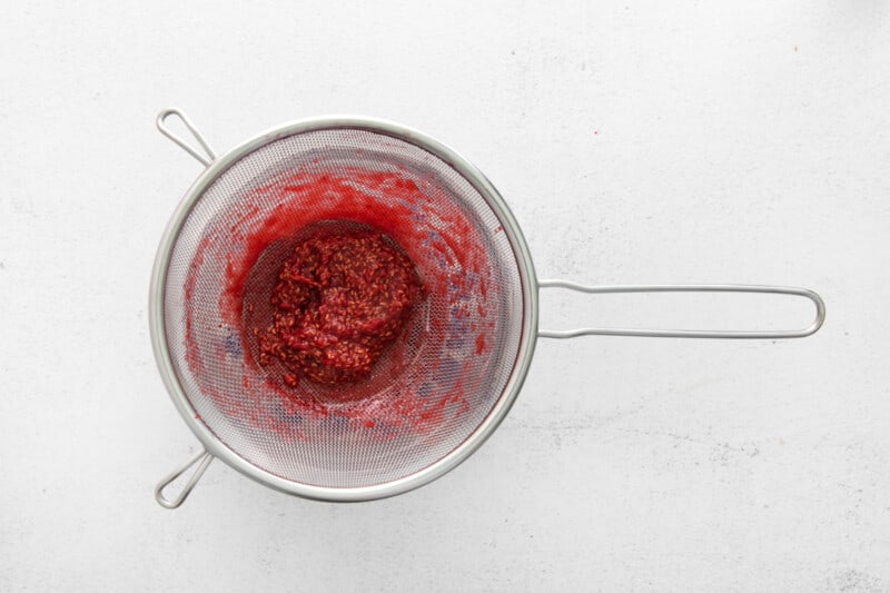 raspberry jam in a sieve set over a saucepan.