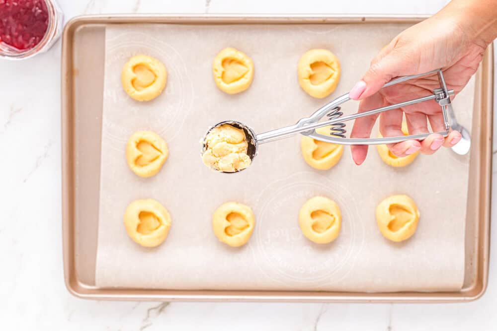 a hand using a cookie scoop to portion cookies onto a baking sheet.