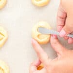 a hand using a butter knife to make heart shaped thumbprints in cookie dough.