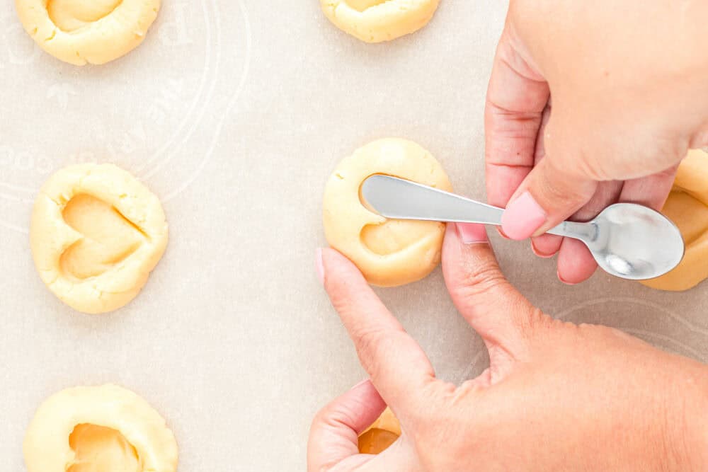 a hand using a butter knife to make heart shaped thumbprints in cookie dough.