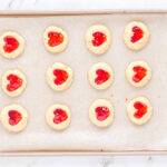 12 heart thumbprint cookies on a baking sheet.