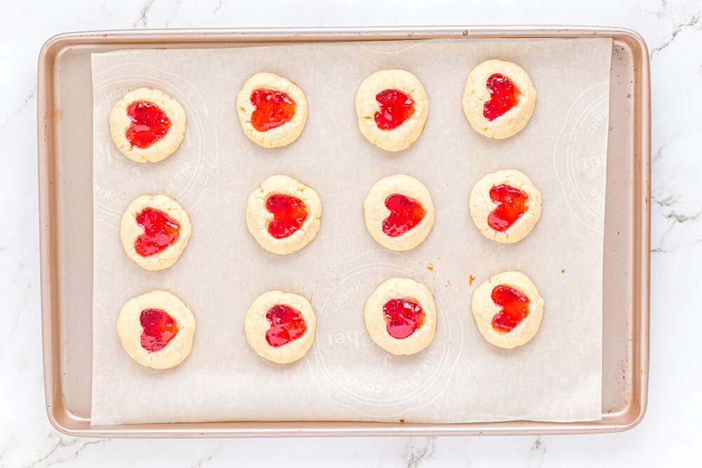 12 heart thumbprint cookies on a baking sheet.