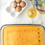 a hand using a wooden spoon to poke holes in baked yellow cake in a rectangular cake pan.