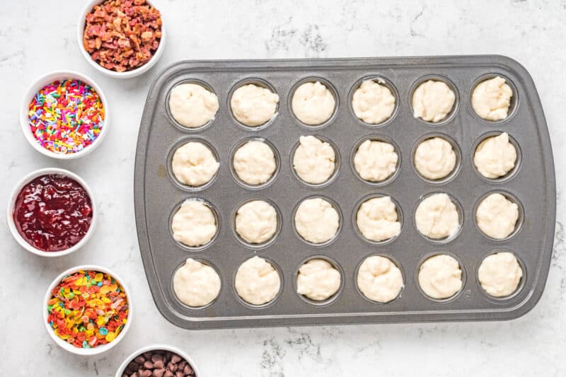 mini muffin tin filled with batter, next to bowls of toppings