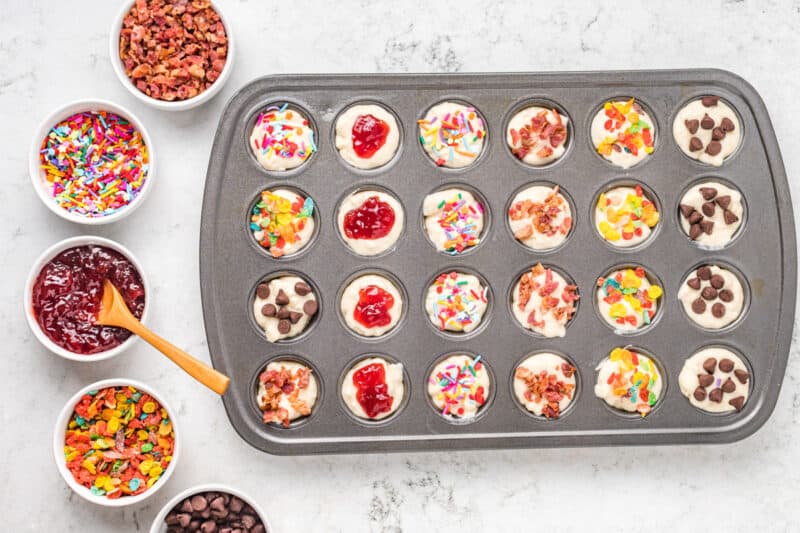 mini muffin tin filled with pancake batter, with a variety of toppings