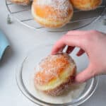 a hand dipping a fried brioche donut into granulated sugar.