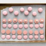 baked raspberry macaron shells on a baking sheet, half flipped over to expose the underside and dolloped with buttercream.