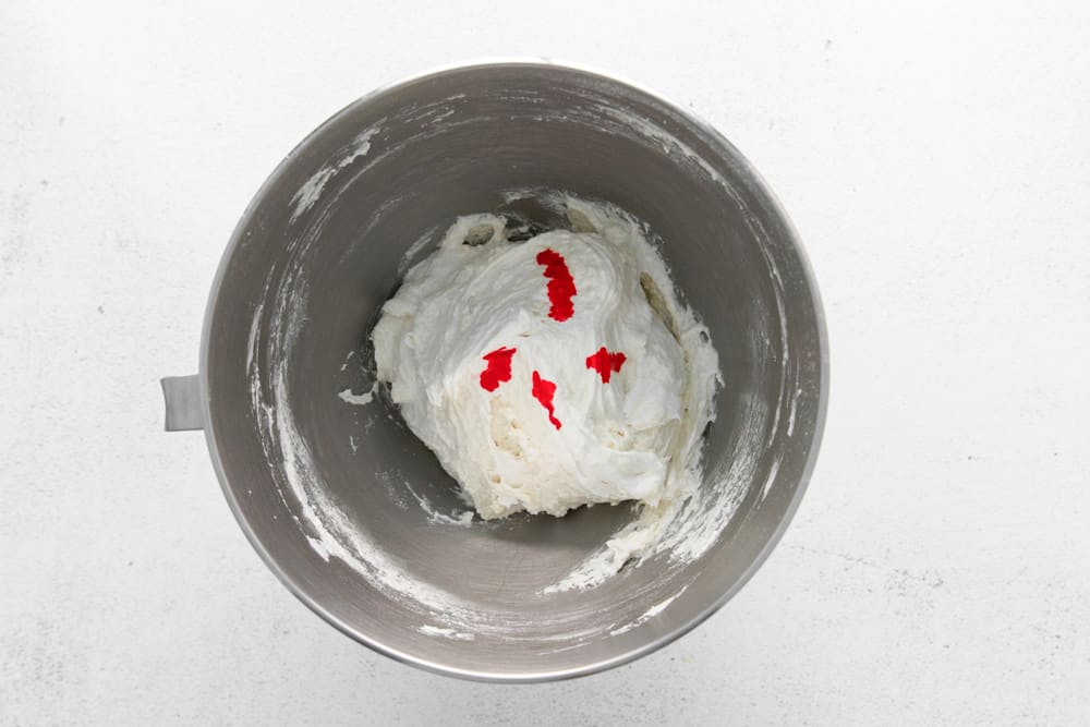 pink food coloring added to meringue batter in a stainless mixing bowl.