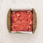 overhead view of cheesecake swirled into red velvet brownie batter in a square baking pan.