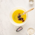 vanilla added to red velvet cheesecake brownie batter in a white bowl.