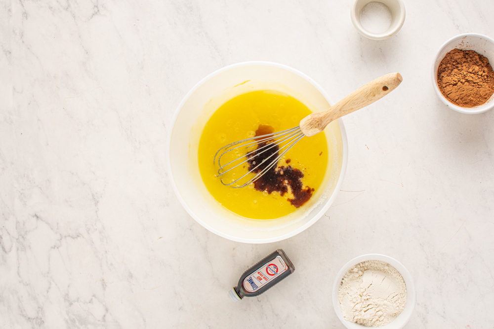 vanilla added to red velvet cheesecake brownie batter in a white bowl.