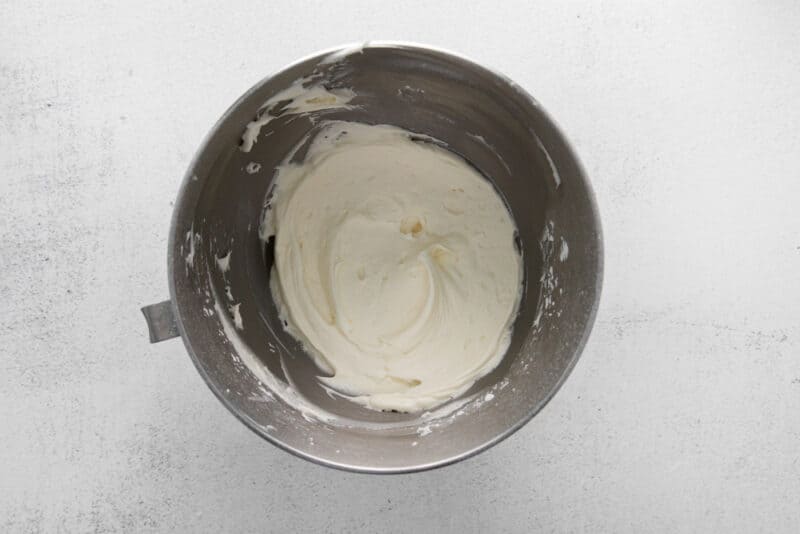 whipped cream in a metal mixing bowl on a white background.