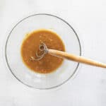 overhead view of wet ingredients for peanut butter granola in a glass bowl with a dough whisk.