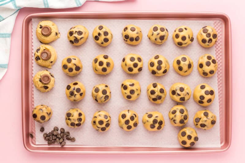 chocolate chip cookie dough balls being stuffed with rolo candies on a baking sheet.