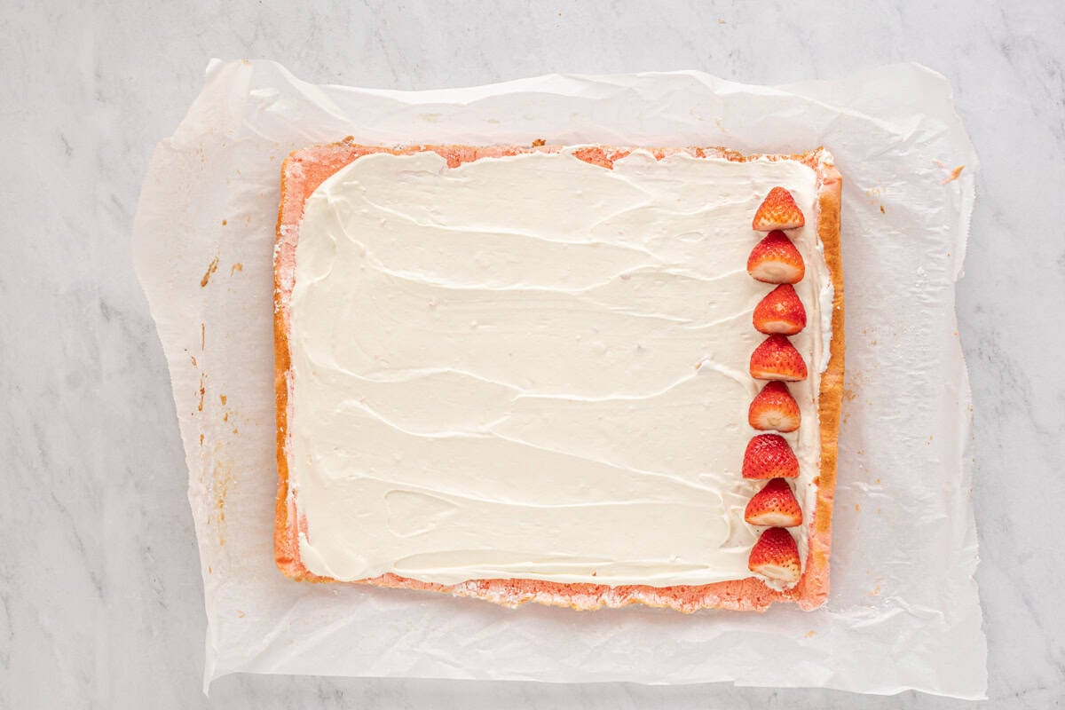strawberry cake covered with cream cheese filling and a thin line of strawberries on the far right side.