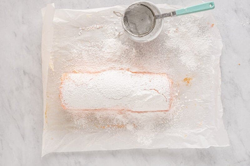 strawberry roll cake topped with paper doilies, covered in powdered sugar.