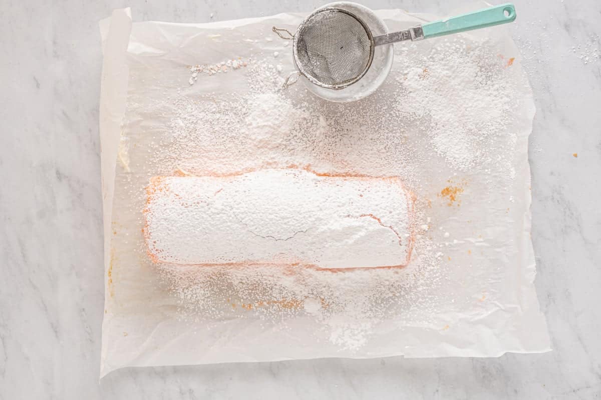 strawberry roll cake topped with paper doilies, covered in powdered sugar.