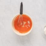 whisking egg yolks, sugar, and strawberry jello in a white bowl.